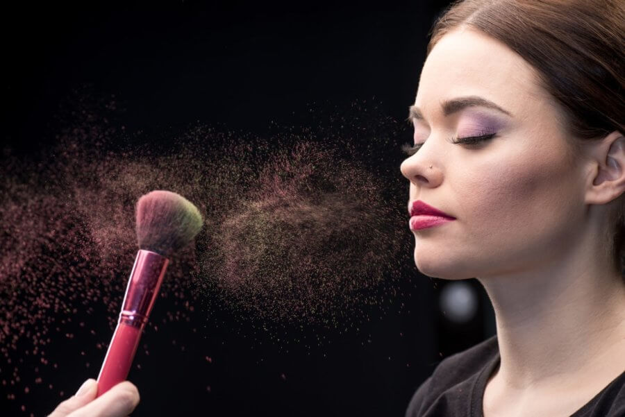Make-up artist sprinkling model's face with powder with help of brush on black