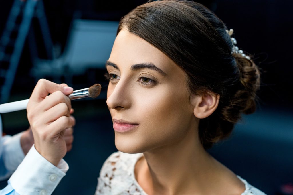 portrait of young woman getting makeup done by makeup artist